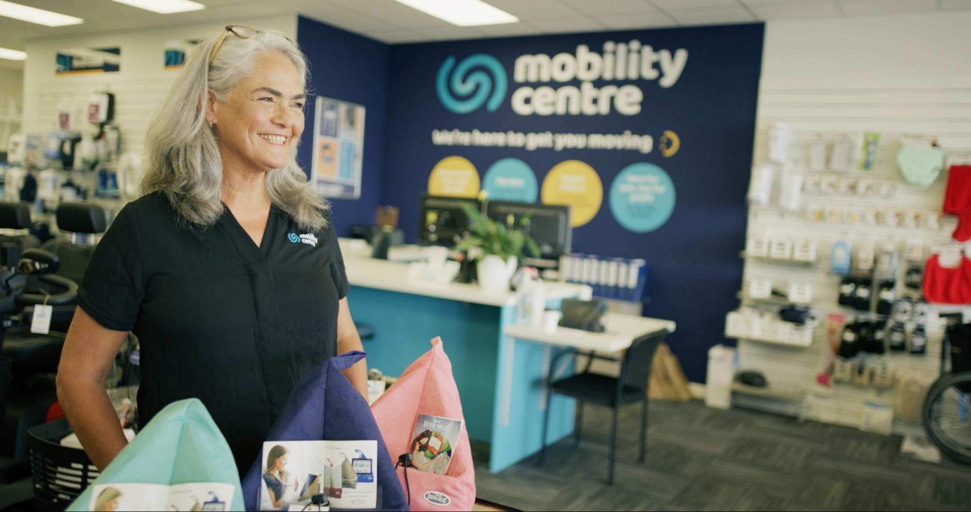 A smiling grey-haired lady greets customers arriving to talk to a mobility specialist